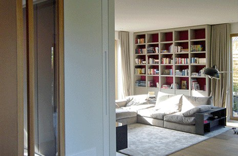 Wohnraum mit roter Bücherwand und hellem Sofa